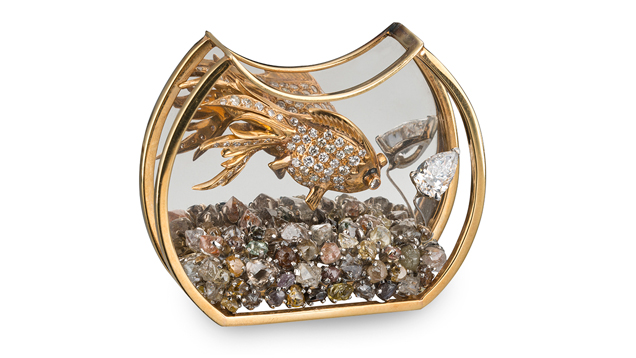 A crescent-shaped bowl with a flat bottom trimmed in gold holds rough diamond gravel and a gold and diamond fish. A crescent-shaped bowl with a flat bottom trimmed in gold holds rough diamond gravel and a gold and diamond fish.