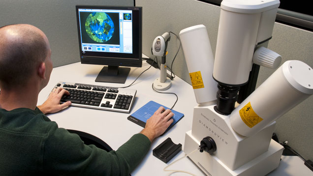 A person is working at a computer with a microscope setup, analyzing data displayed on the screen.