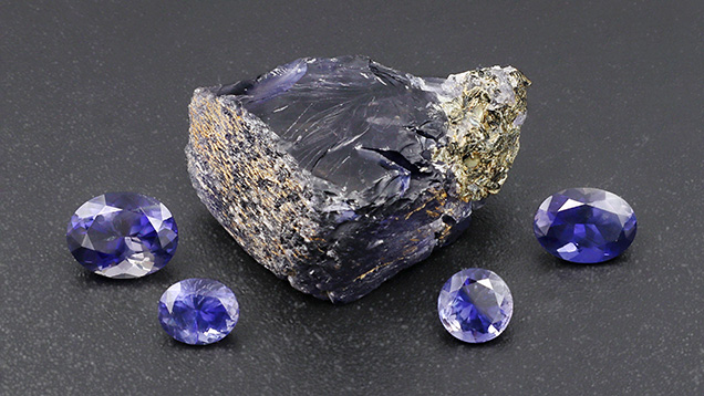 Figure 12. Rough and cut iolite from Blue Bear. From left to right, the faceted stones weigh 1.24, 0.48, 0.48, and 0.88 ct. Photo by Philippe Belley. Figure 12. Rough and cut iolite from Blue Bear. From left to right, the faceted stones weigh 1.24, 0.48, 0.48, and 0.88 ct. Photo by Philippe Belley.