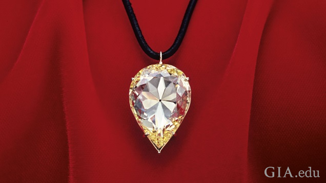 A large pear shaped yellow diamond hangs from a black cord and lies against red material. A large pear shaped yellow diamond hangs from a black cord and lies against red material.