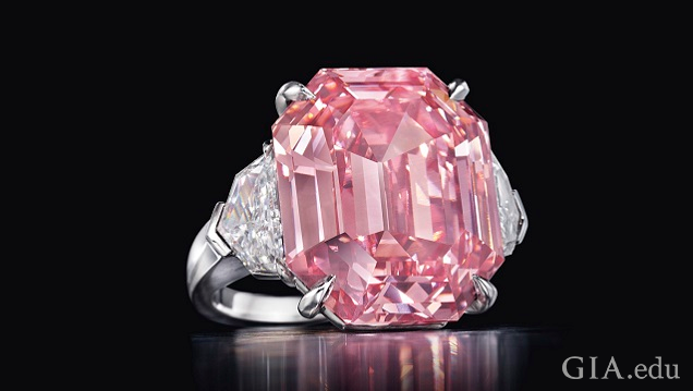 The large pink center stone of this ring is a cut-cornered rectangular-cut diamond. It is flanked by colorless diamonds. The large pink center stone of this ring is a cut-cornered rectangular-cut diamond. It is flanked by colorless diamonds.