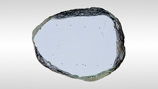 Polished Yogo sapphire wafer sample. Figure 3. A typical polished Yogo wafer sample measuring 0.93 mm thick. The c-axis is perpendicular to the wafer surface. Note the distinct color uniformity and the lack of any color zoning. Ten LA-ICP-QMS measurement points can also be seen on this wafer. Photo by John L. Emmett.