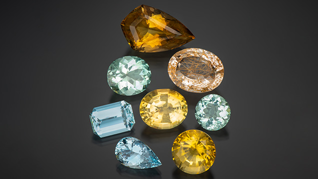 Figure 1. Some of Virtu Gem’s larger gemstones from Kenya, Malawi, and Zambia at the Ethical Gem Fair. Clockwise from top: 45.00 ct citrine, 32.33 ct rutilated quartz, 9.80 ct aquamarine, 21.65 ct citrine, 9.99 ct aquamarine, 12.32 ct aquamarine, 17.20 ct aquamarine, and 20.15 ct citrine (center). Photo by Robert Weldon; courtesy of Virtu Gem. Figure 1. Some of Virtu Gem’s larger gemstones from Kenya, Malawi, and Zambia at the Ethical Gem Fair. Clockwise from top: 45.00 ct citrine, 32.33 ct rutilated quartz, 9.80 ct aquamarine, 21.65 ct citrine, 9.99 ct aquamarine, 12.32 ct aquamarine, 17.20 ct aquamarine, and 20.15 ct citrine (center). Photo by Robert Weldon; courtesy of Virtu Gem.
