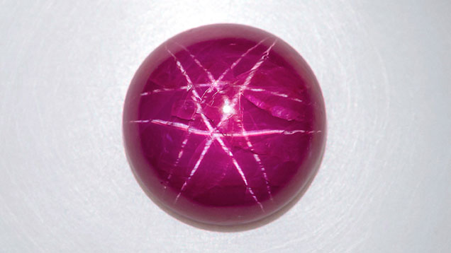 Figure 1. This unheated 11.43 ct purplish red round ruby cabochon displayed a white double-star phenomenon. Photo by Nuttapol Kitdee. Figure 1. This unheated 11.43 ct purplish red round ruby cabochon displayed a white double-star phenomenon. Photo by Nuttapol Kitdee.