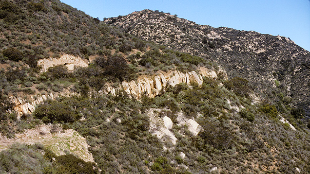 Figure 5. The light-colored rock is the outcrop exposure of a cross section of the westward-dipping Stewart pegmatite dike, located north of the small town of Pala in northern San Diego County, California. Photo by James E. Shigley. Figure 5. The light-colored rock is the outcrop exposure of a cross section of the westward-dipping Stewart pegmatite dike, located north of the small town of Pala in northern San Diego County, California. Photo by James E. Shigley.