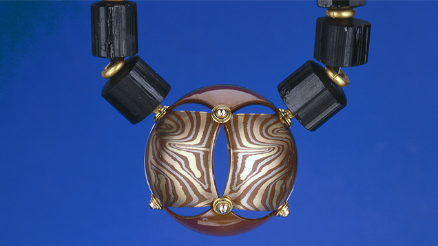 This mokume gane pendant, made of patinaed copper and 14K yellow, red and grey gold, hangs on a black tourmaline crystal bead and 22K gold rondell necklace. Mokume gane is a technique of layering metals. Created by George Sawyer. Photo by Robert Weldon/GIA, gift of George Sawyer. This mokume gane pendant, made of patinaed copper and 14K yellow, red and grey gold, hangs on a black tourmaline crystal bead and 22K gold rondell necklace. Mokume gane is a technique of layering metals. Created by George Sawyer. Photo by Robert Weldon/GIA, gift of George Sawyer.