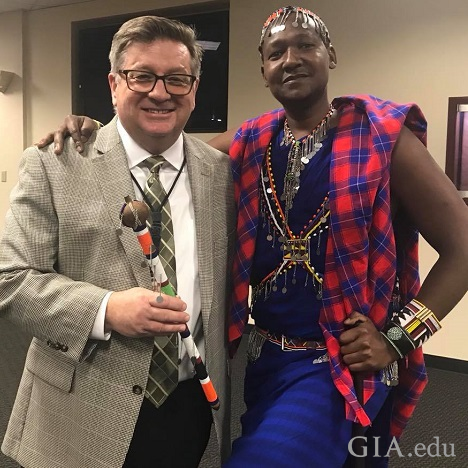 A man in a suit with a man in Masai tribal clothes pose together.