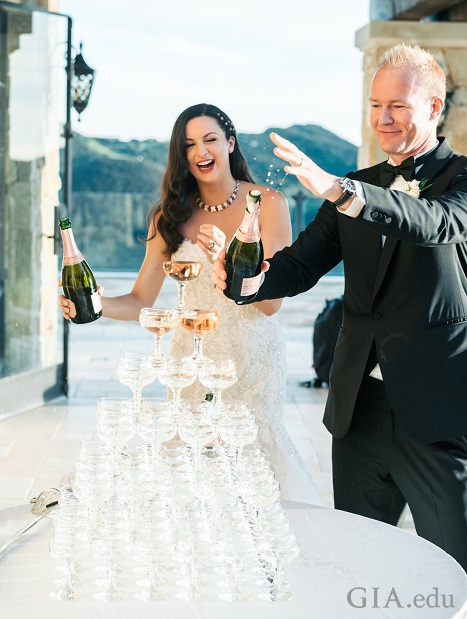 Wedding couple pours champagne over a tower of champagne glasses.